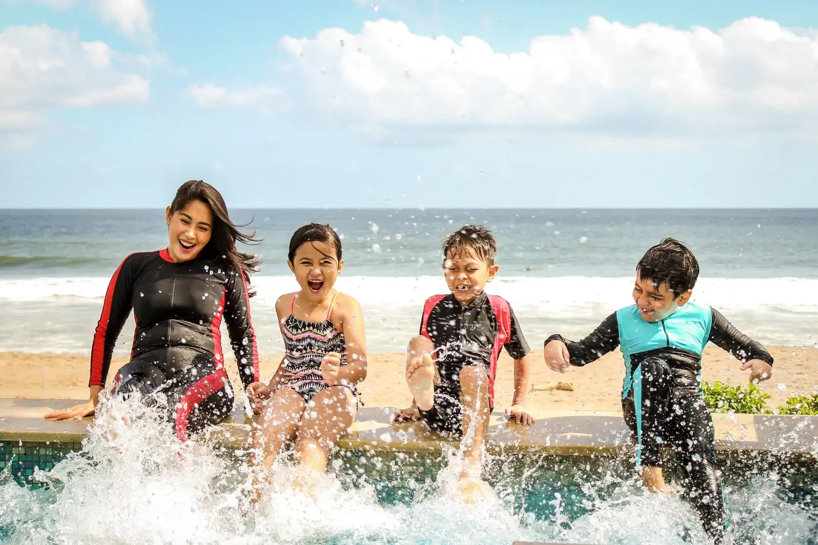 Mother and children in wetsuits splashing in the sea – family surf lessons