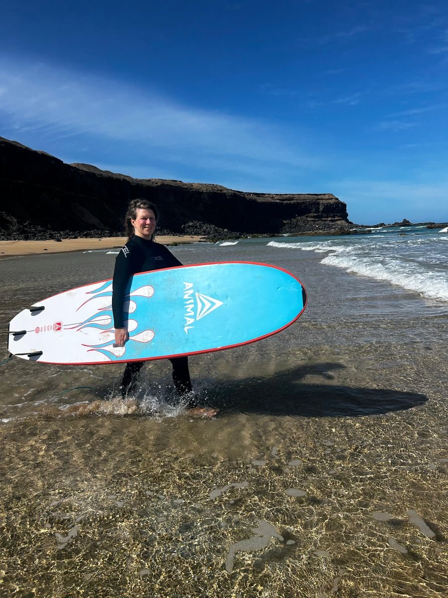Surf student carrying her board through the shallows in Fuerteventura
