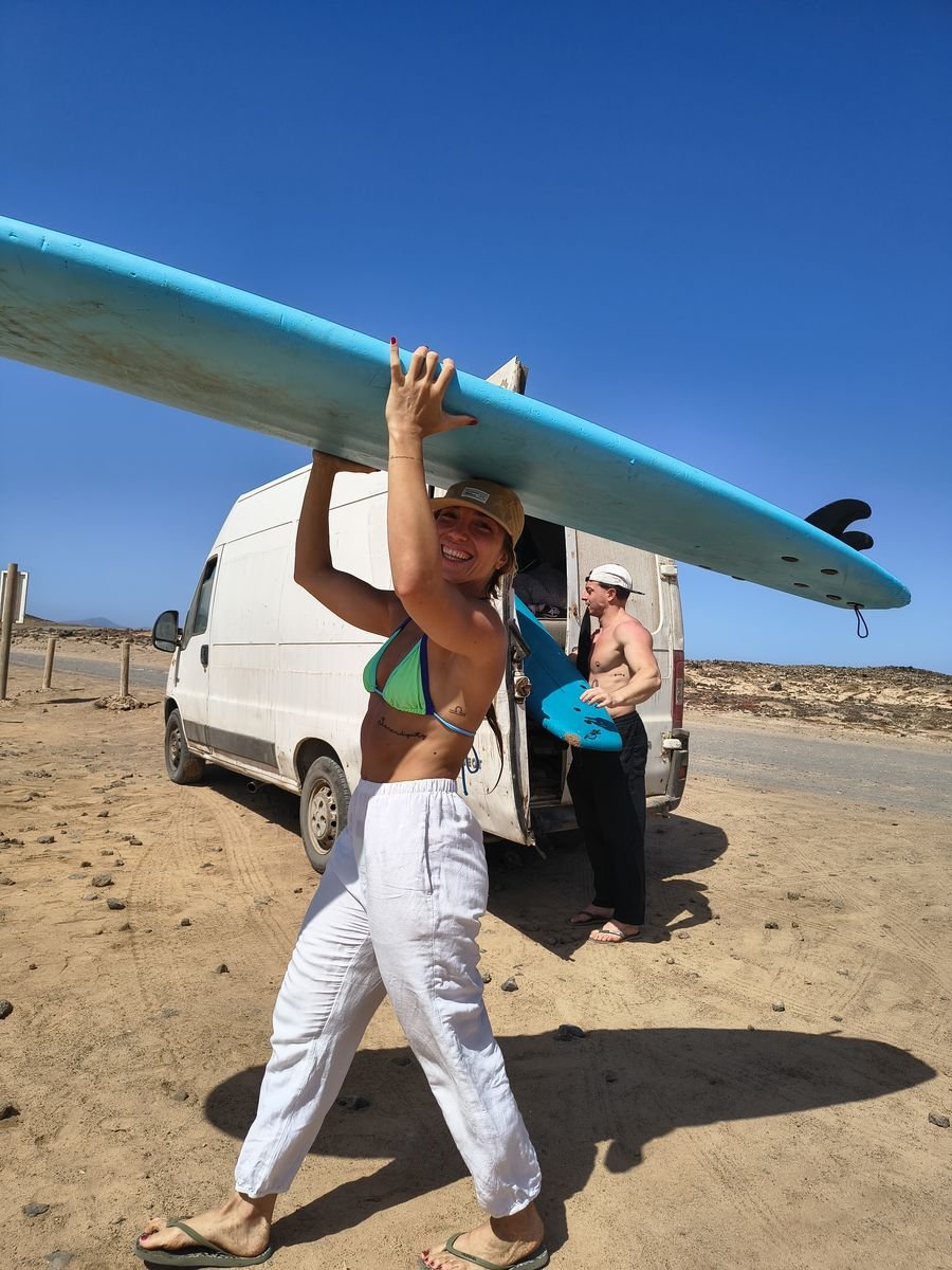 Surf student carrying a surfboard on her head next to the surf van
