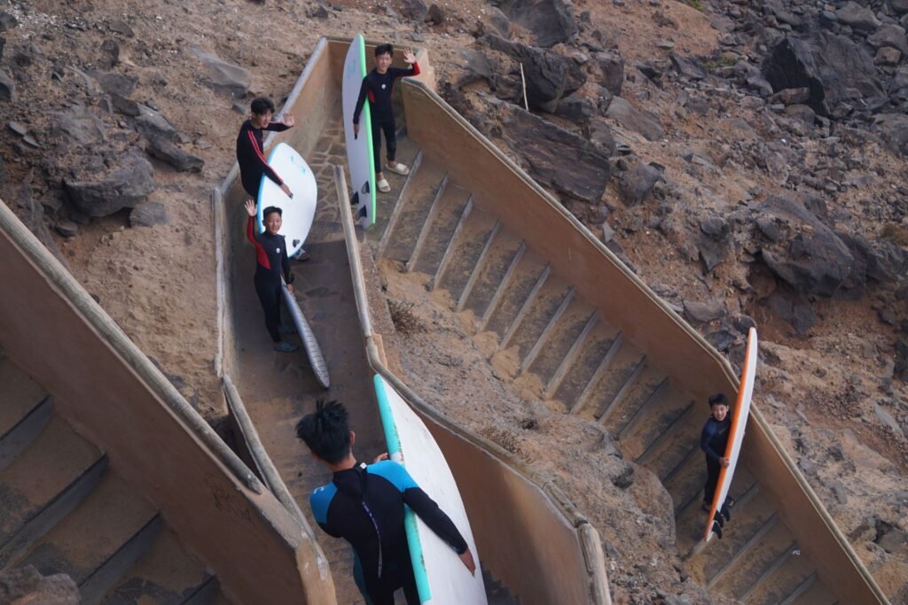 Surf students carrying boards down the cliff stairs to the beach in Fuerteventura