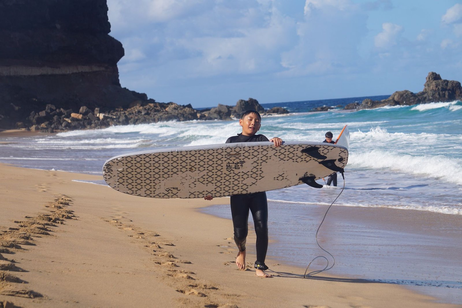 Young surfer carrying a surfboard out of the water after a lesson in Fuerteventura
