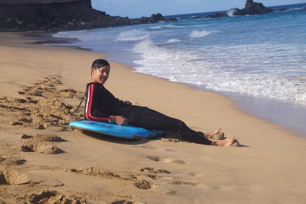 Smiling surf student lying on his board on the sand after a lesson