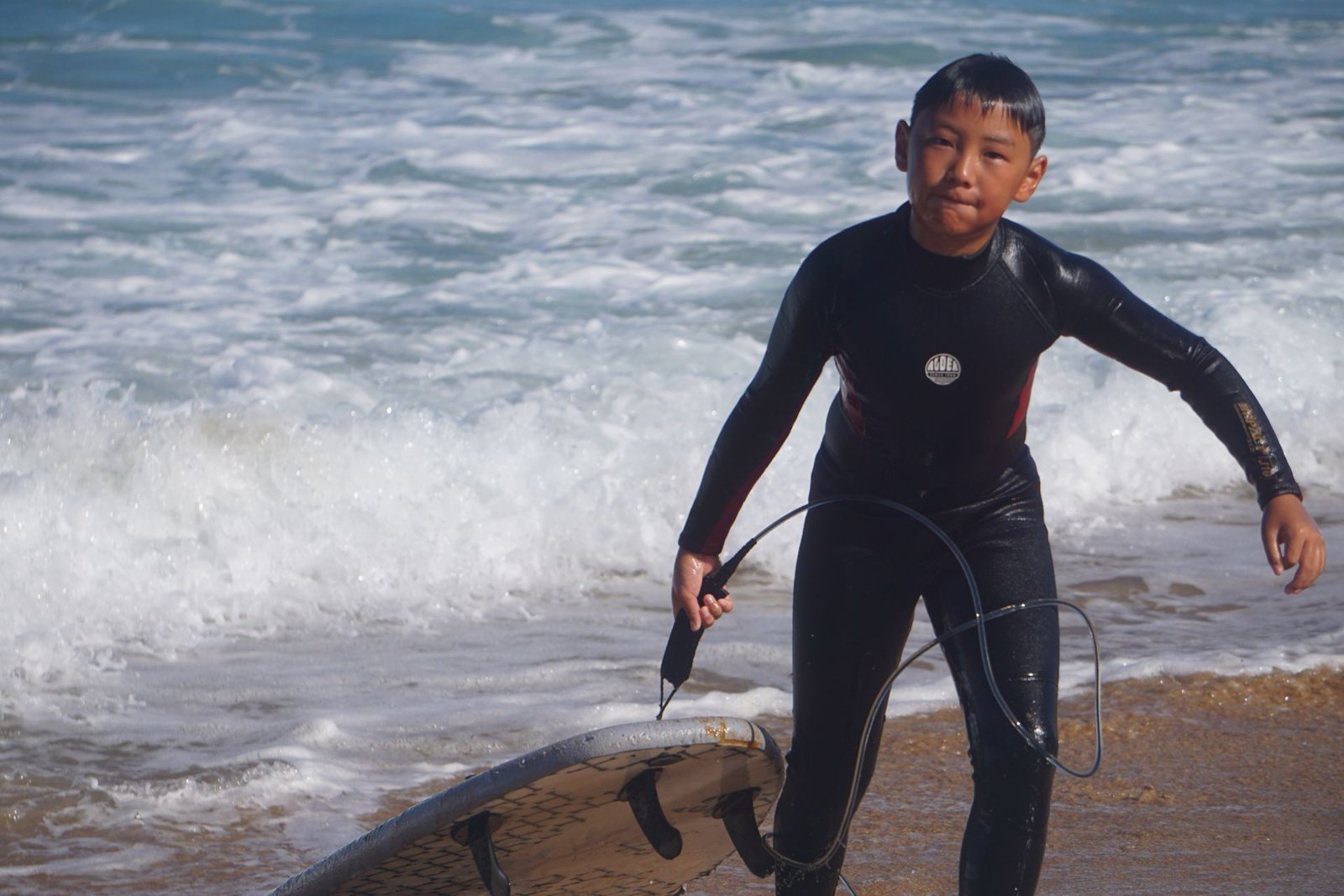 Happy young surfer walking out of the waves with his board leash