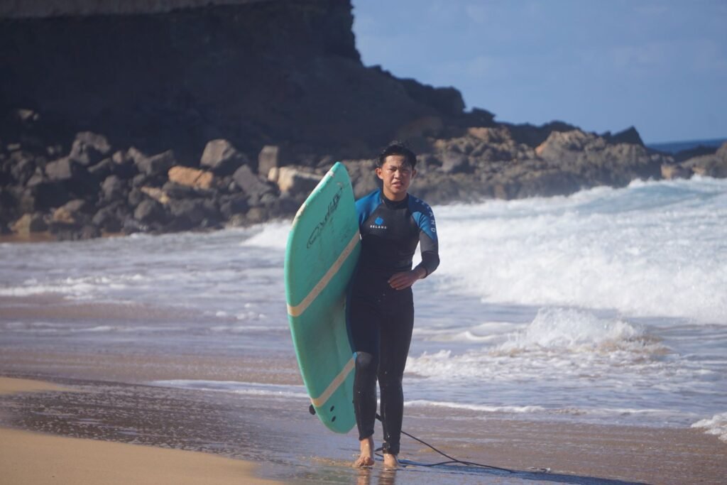 Teen surfer carrying a green surfboard along the beach after a lesson