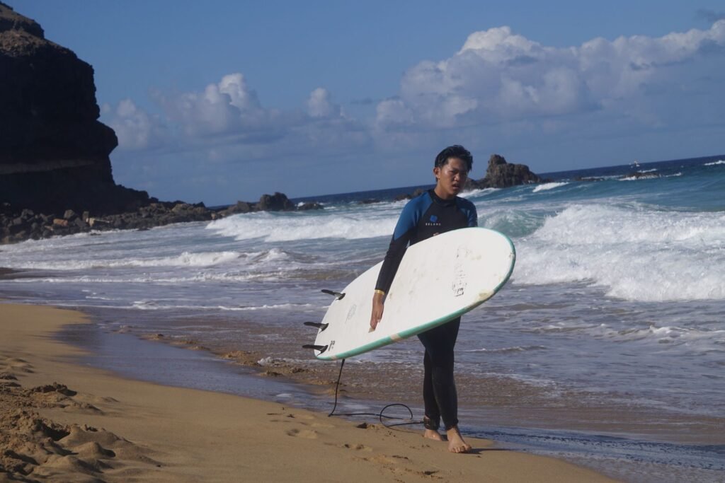 Surf student carrying a white surfboard along the shoreline, Fuerteventura
